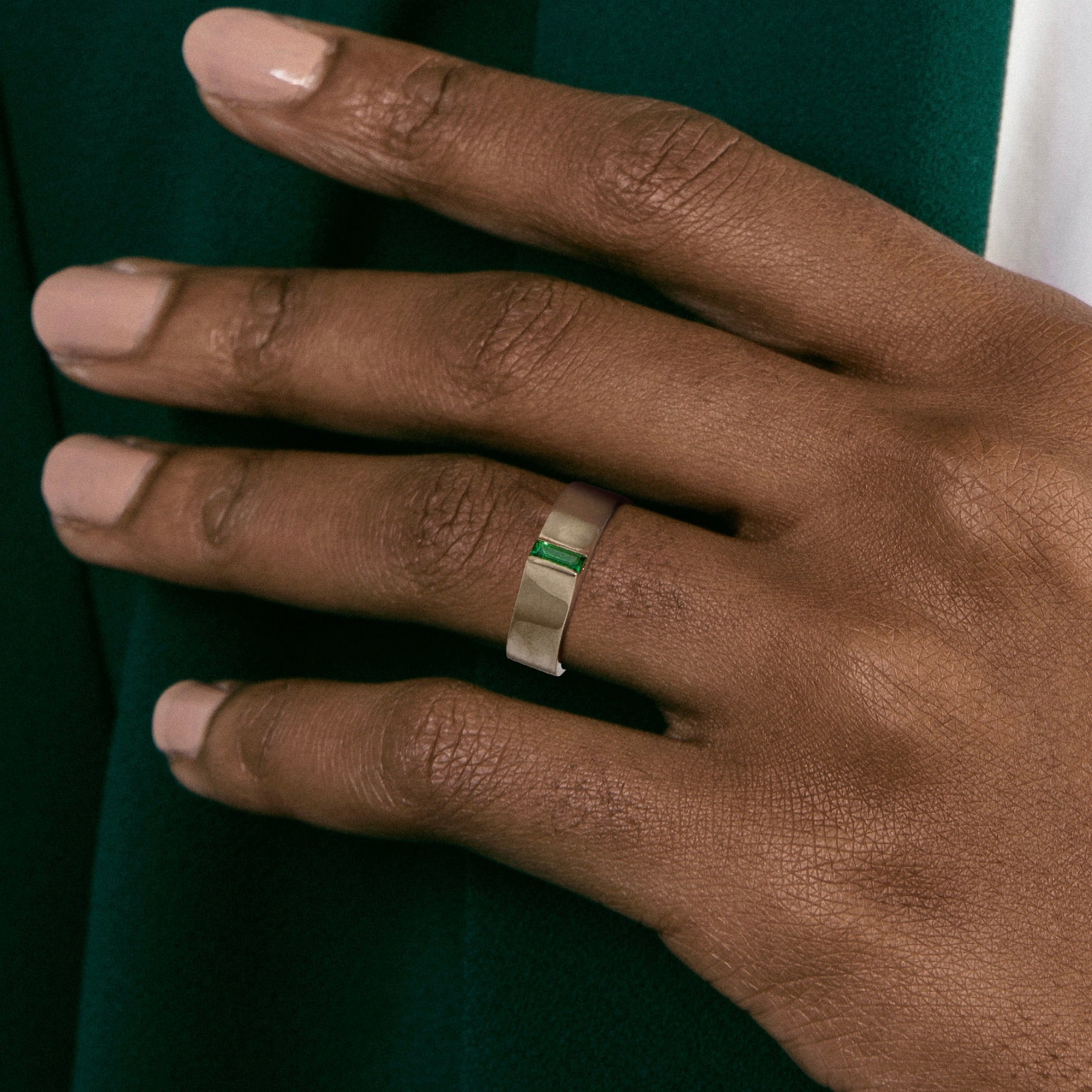 Flat gold band with exposed green baguette gemstone shown worn in natural light