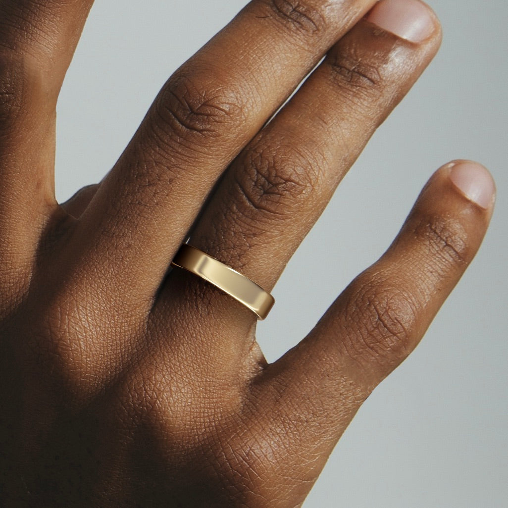 Wide flat gold wedding band worn on hand