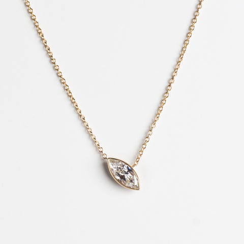 A delicate gold chain necklace featuring a  marquise-shaped pendant set with a lab-grown white diamond, displayed against a clean, light gray background.