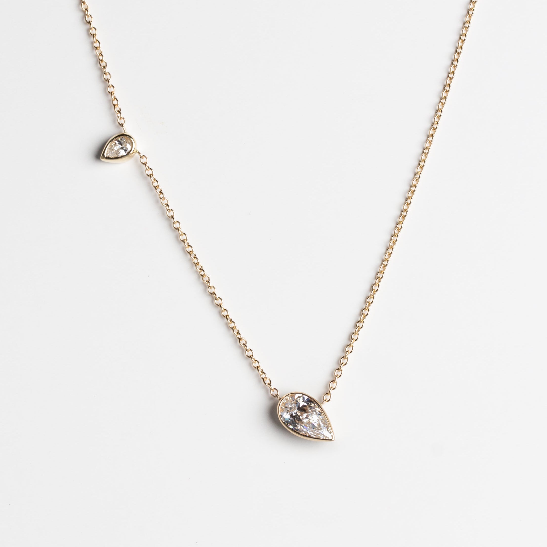A gold chain necklace featuring two pear-shaped white lab-grown diamonds, one larger pendant and one smaller accent stone, displayed on a clean white background.