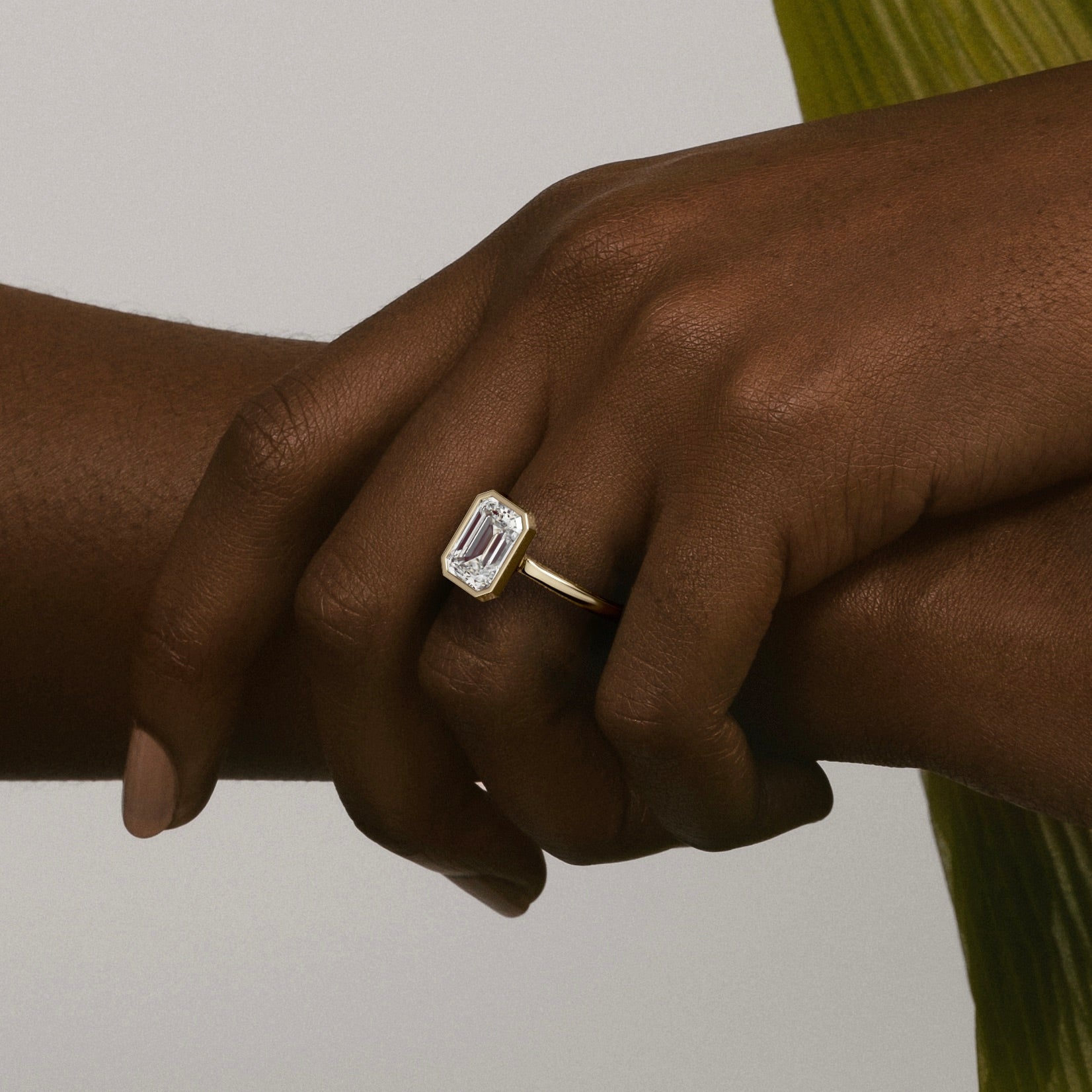 close view of 2.50 ct emerald-cut diamond bezel engagement ring on thin domed band worn on hand