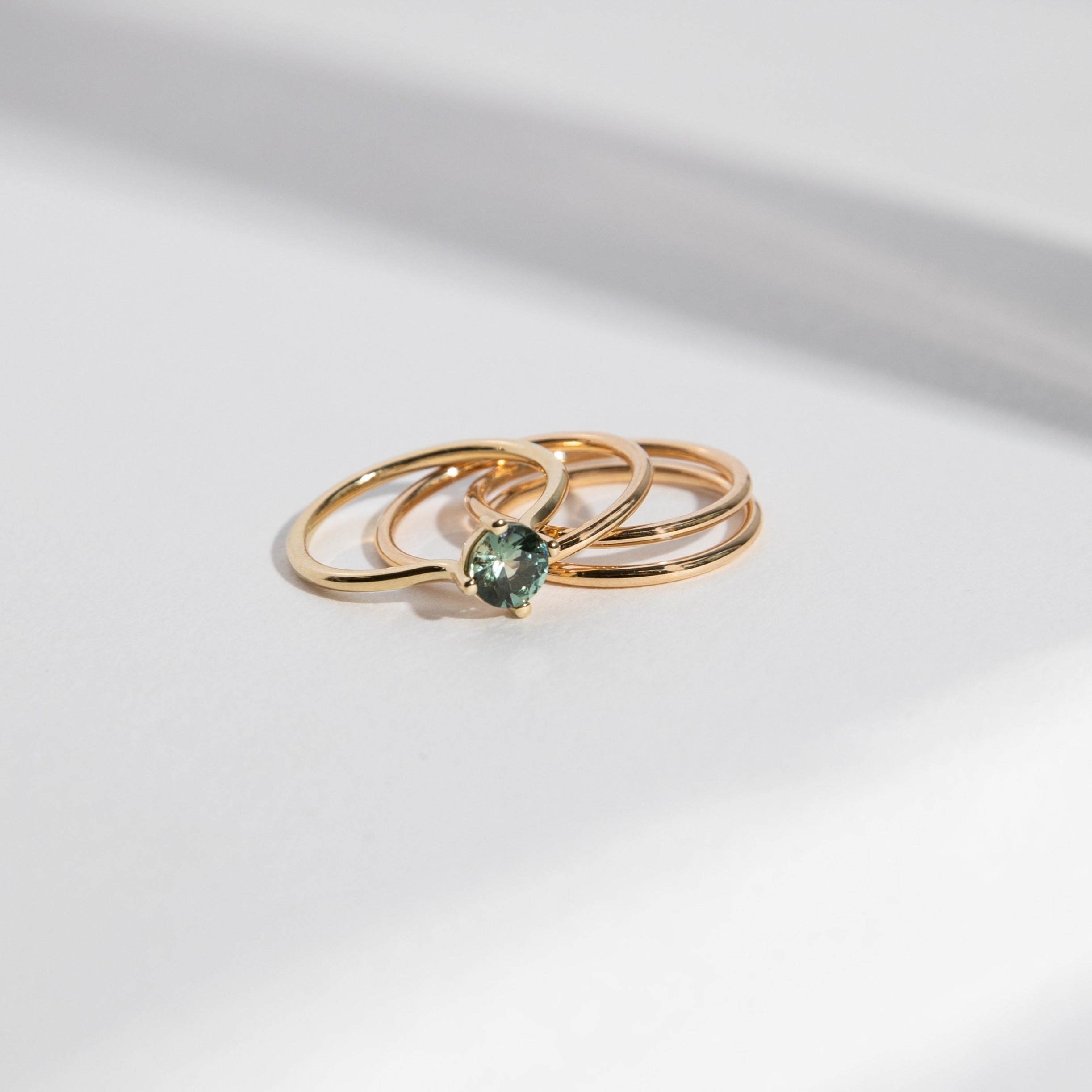 Three thin gold bands placed beside a sapphire engagement ring