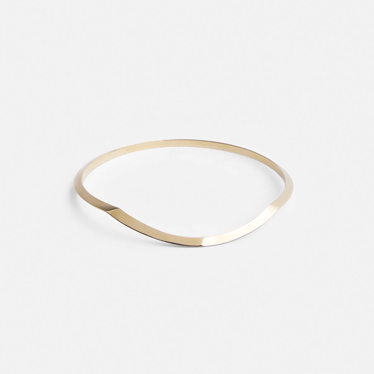 yellow brass bangle bracelet with tapered lines and curved sculptural silhouette shown from the front