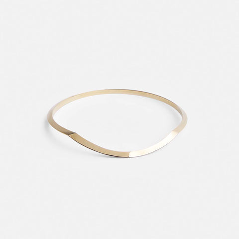 yellow brass bangle bracelet with tapered lines and curved sculptural silhouette shown from the front