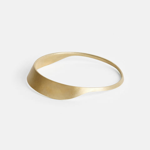 side profile of yellow brass bangle with sleek curved silhouette and minimal design