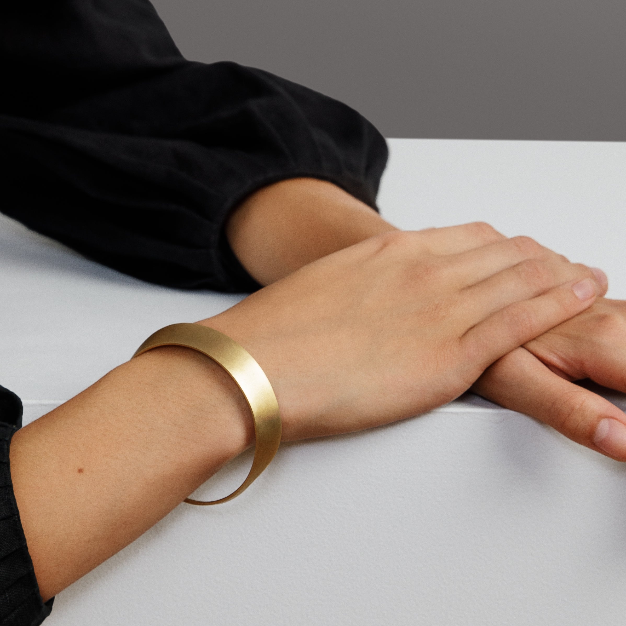 yellow brass bangle bracelet with curved sculptural form worn on wrist