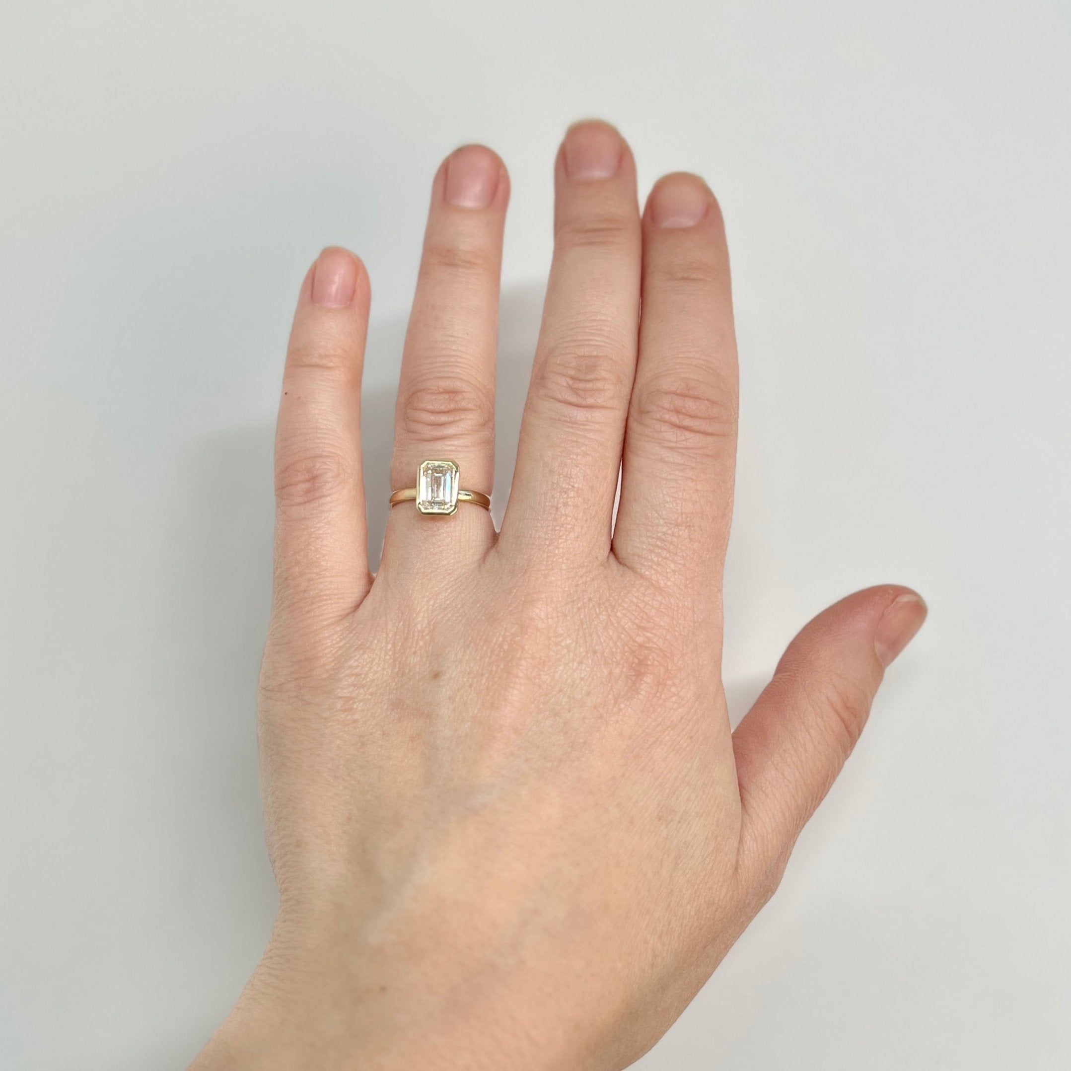 Minimal Domed Bezel Setting Engagement Ring with 1.5ct lab grown emerald cut diamond in 14 karat yellow gold SHW fine jewelry stores in NYC