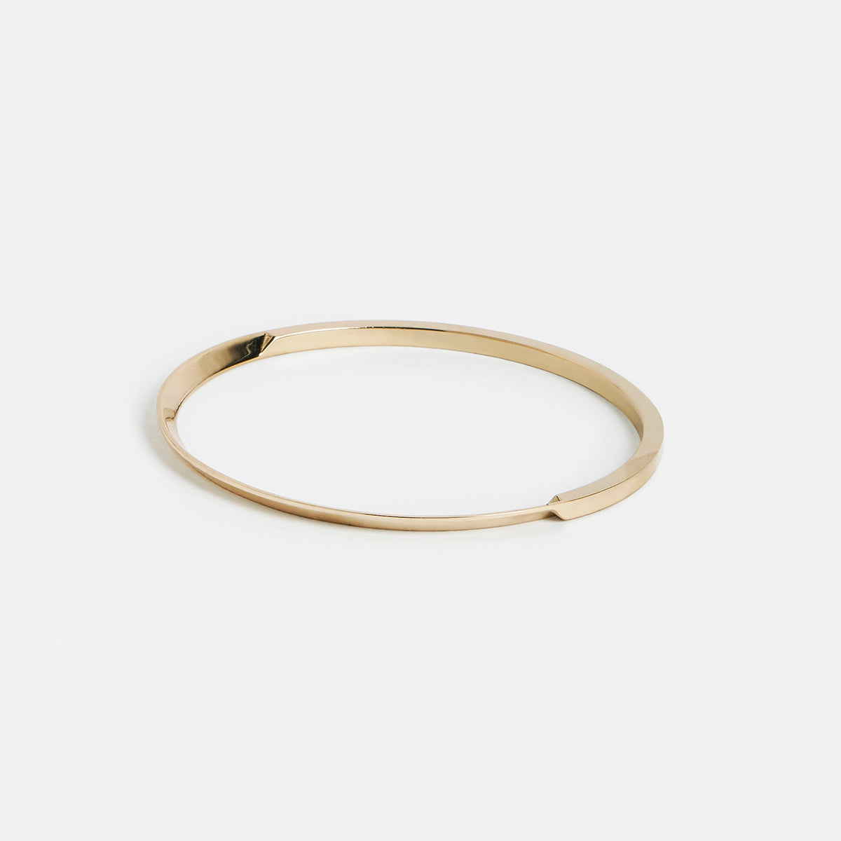 yellow brass bangle bracelet with tapered curved lines shown from an angled side perspective