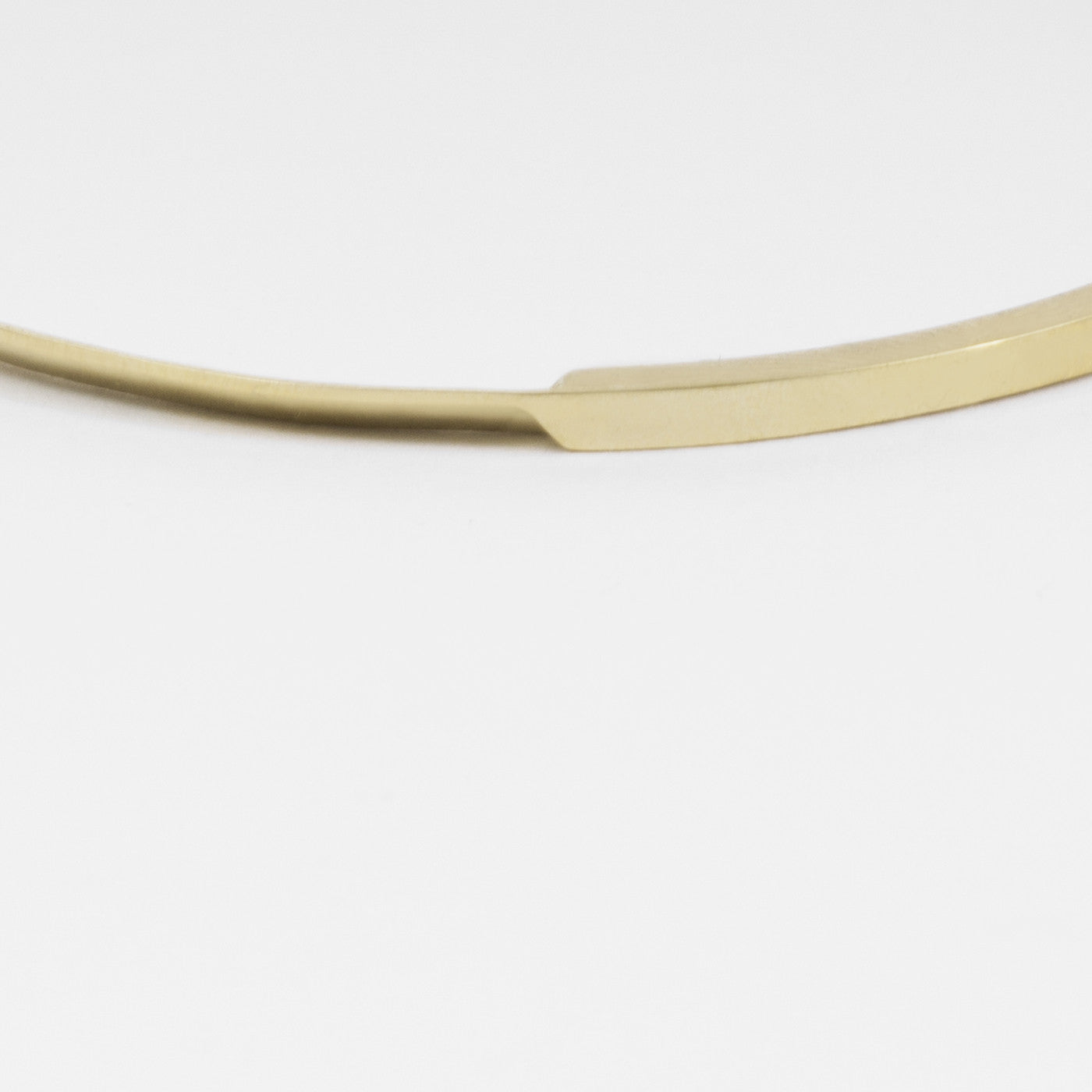 close-up of yellow brass bangle highlighting tapered curves and polished sculptural surface