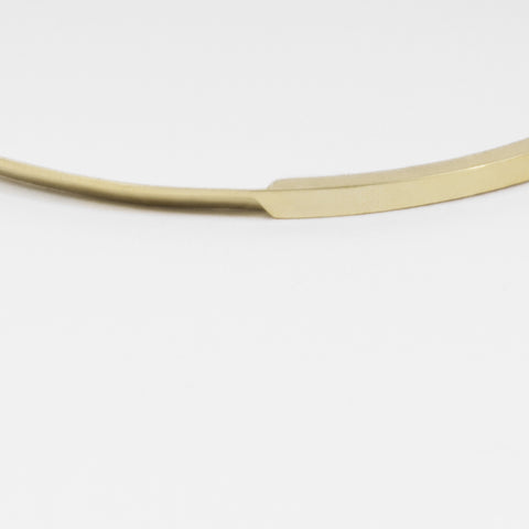 close-up of yellow brass bangle highlighting tapered curves and polished sculptural surface
